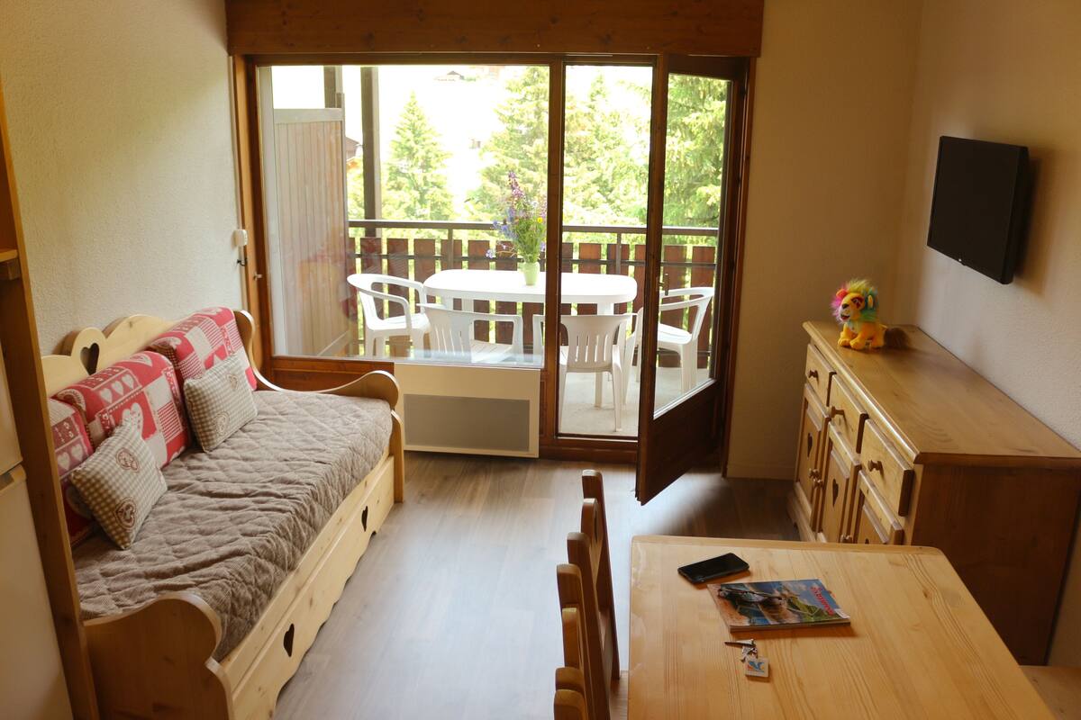 Une pièce confortable avec un lit en bois, une petite table et un téléviseur fixé au mur.