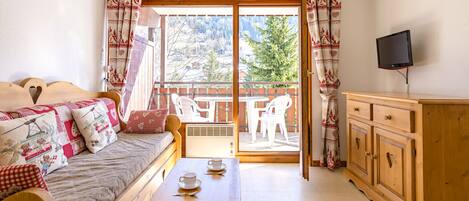 A cozy room with a wooden bed, a table with cups, a TV, and a balcony with chairs.