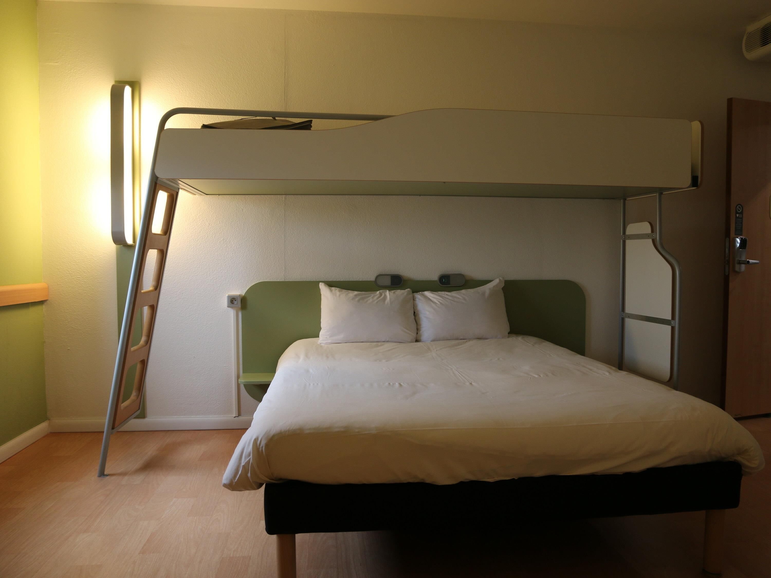 A bunk bed with a ladder, a bedside table, and a wall-mounted light fixture.