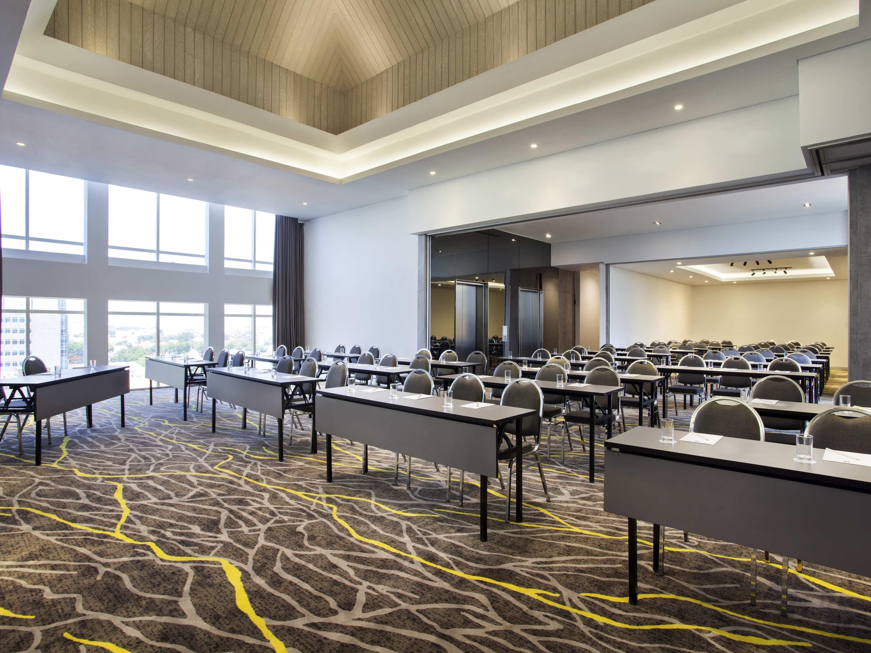 A conference room with multiple tables and chairs, large windows, and a patterned carpet.