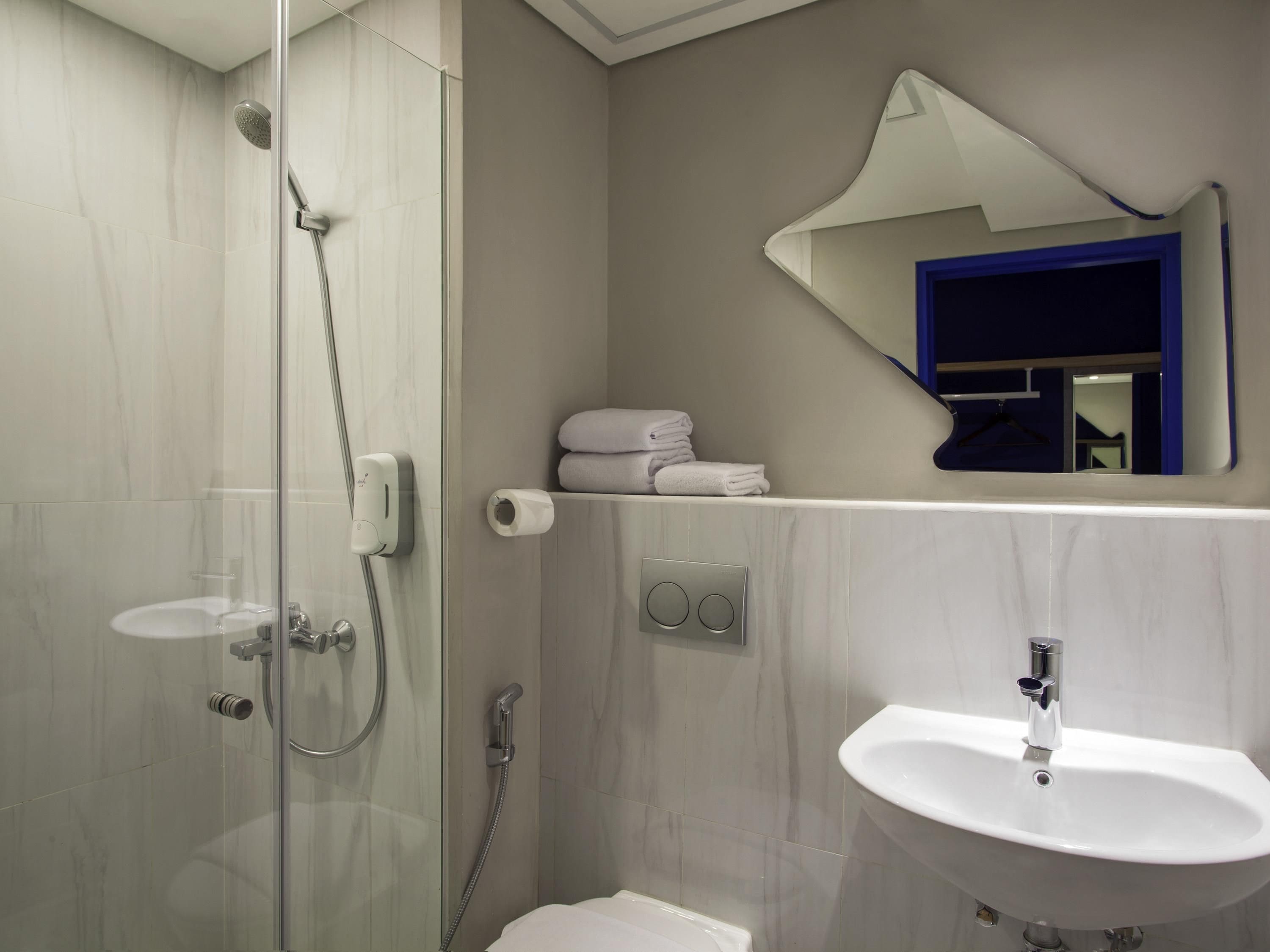 Un bagno moderno con doccia vetrata, lavandino bianco e specchio sopra al lavandino.