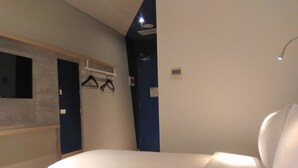 Un dormitorio con cama, perchero en la pared y una ventana pequeña.