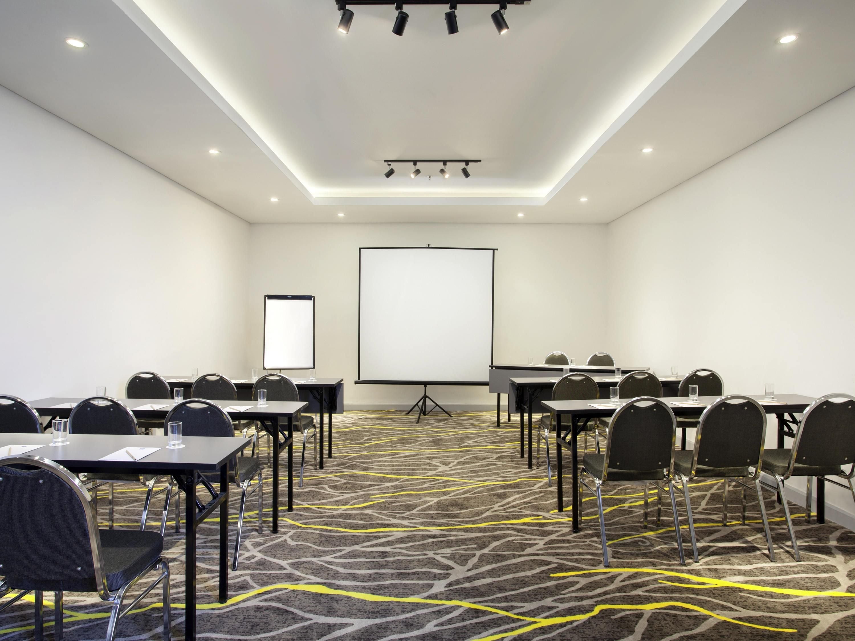 A conference room with tables, chairs, a projector screen, and a carpeted floor.