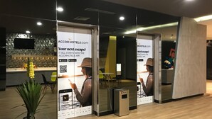 A modern hotel lobby with a reception desk, a potted plant, and promotional posters for the AccorHotels app. - ibis budget Surabaya Diponegoro (Surabaya)