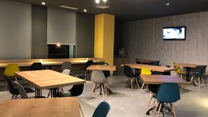 A modern conference room with wooden tables and chairs, a large screen for presentations, and a minimalist design with neutral walls and a yellow accent wall. - ibis budget Surabaya Diponegoro (Surabaya)