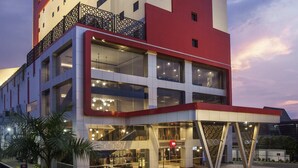 Un hotel de varios pisos con fachada roja y blanca, grandes ventanales y un restaurante visible en la planta baja.
