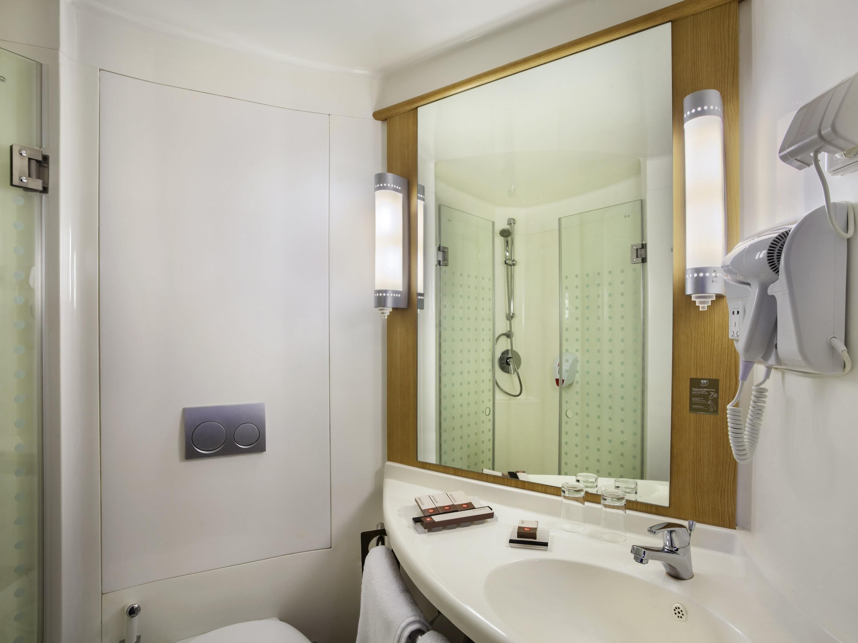 A bathroom with a large mirror, a hairdryer, a sink, and a shower.