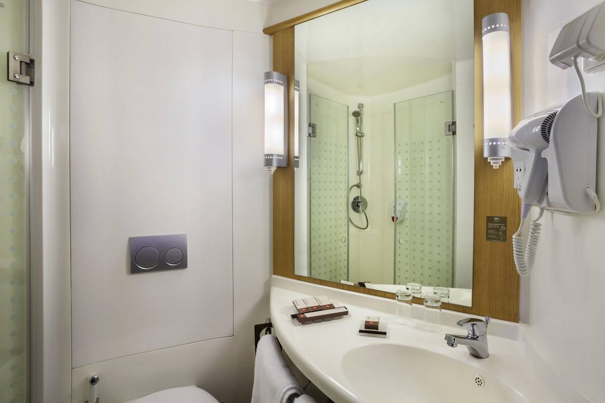 A bathroom with a large mirror, a hairdryer, a sink, and a shower.
