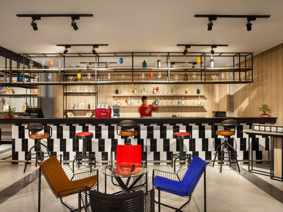 A modern bar area with multiple stools, a counter, and shelves stocked with bottles and glasses.