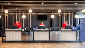Una recepción con tres empleados en uniformes rojos, un televisor de pantalla plana sobre el mostrador y un cartel que indica 'Bienvenida Prioritaria'.