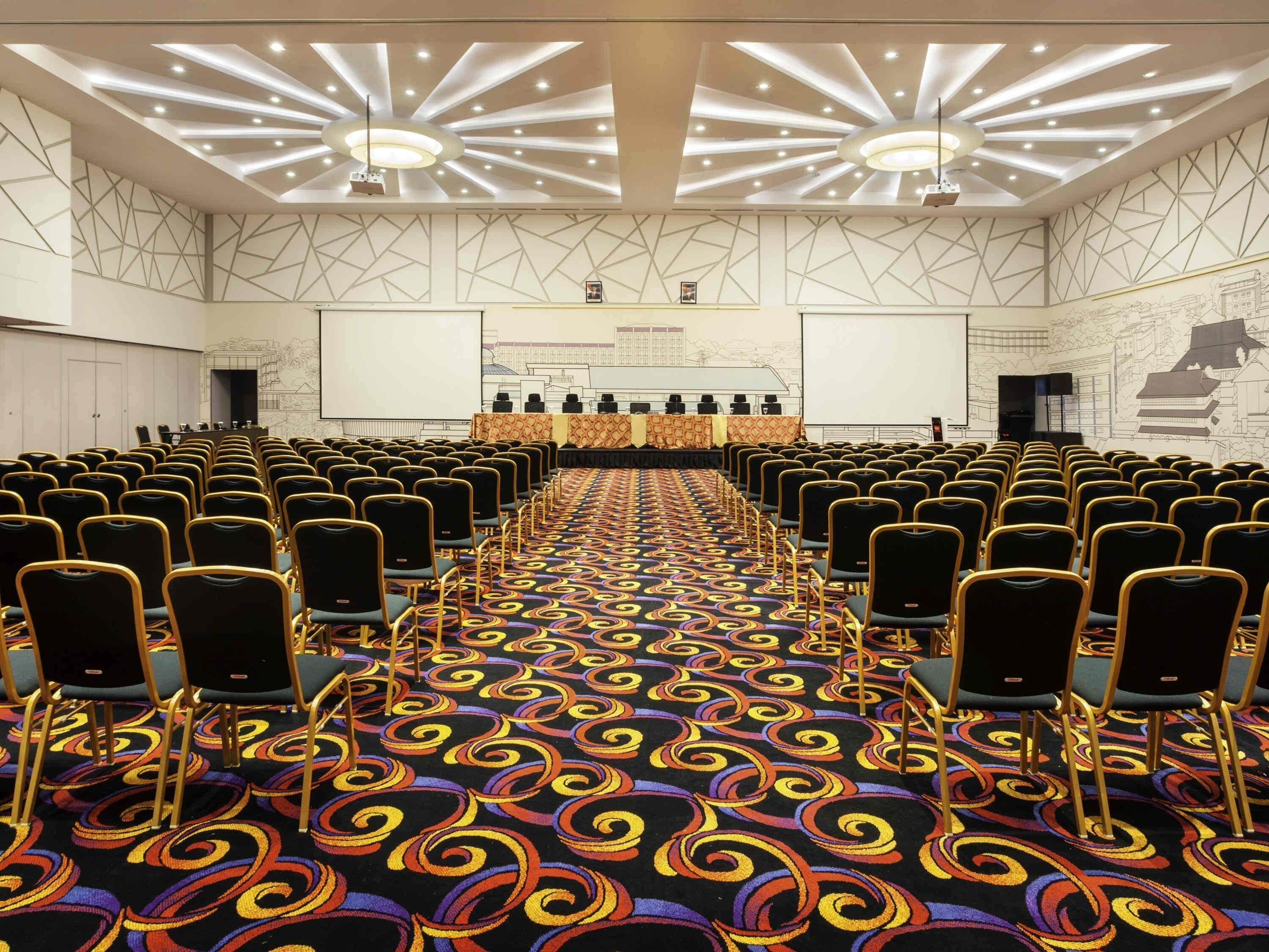 A conference room with rows of chairs, a patterned carpet, and a ceiling with recessed lighting.