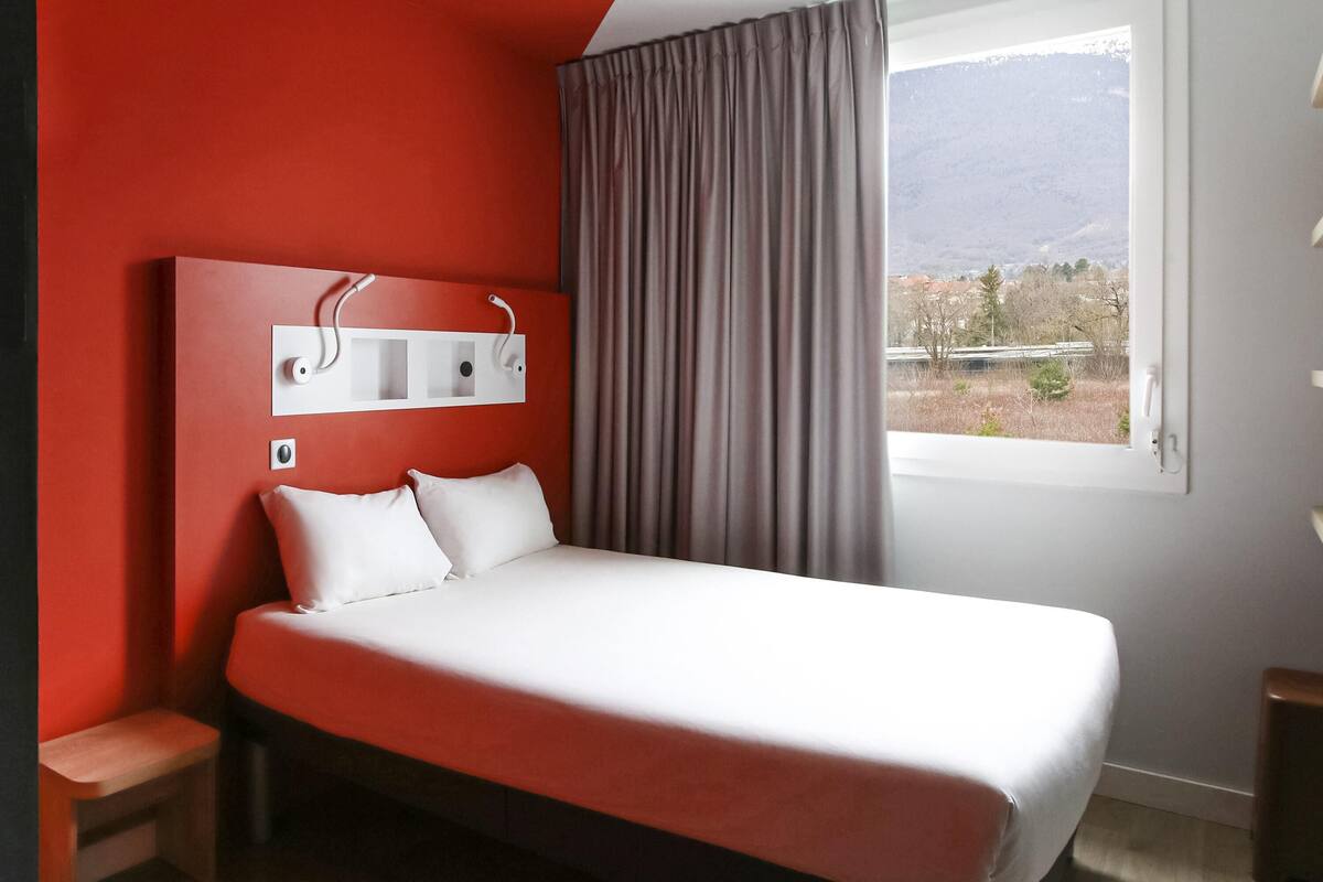 Une chambre à coucher avec un lit, une table de chevet, une fenêtre donnant sur les montagnes et un mur rouge.
