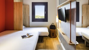 Ein Hotelzimmer mit zwei Betten, einem an der Wand montierten Fernseher, einem Fenster mit Blick und einem kleinen Tisch mit Lampe.