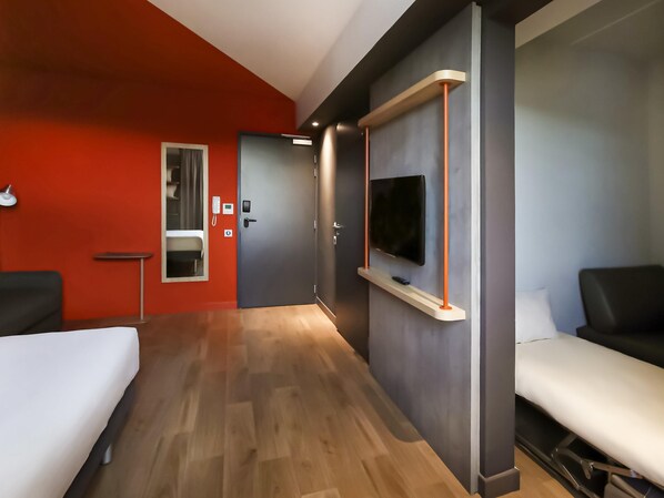 Une chambre d’hôtel comprenant un lit, un bureau, une chaise, un téléviseur fixé au mur et une salle de bain avec un miroir et un lavabo.