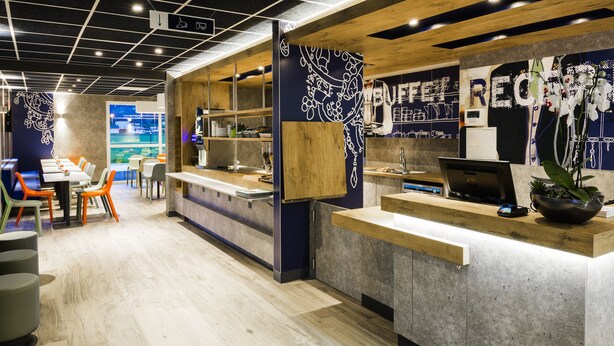 A modern cafe with a wooden counter, seating area, and decorative wall art. - Ibis Budget Saint Genis Pouilly Geneva (Saint-Genis-Pouilly)