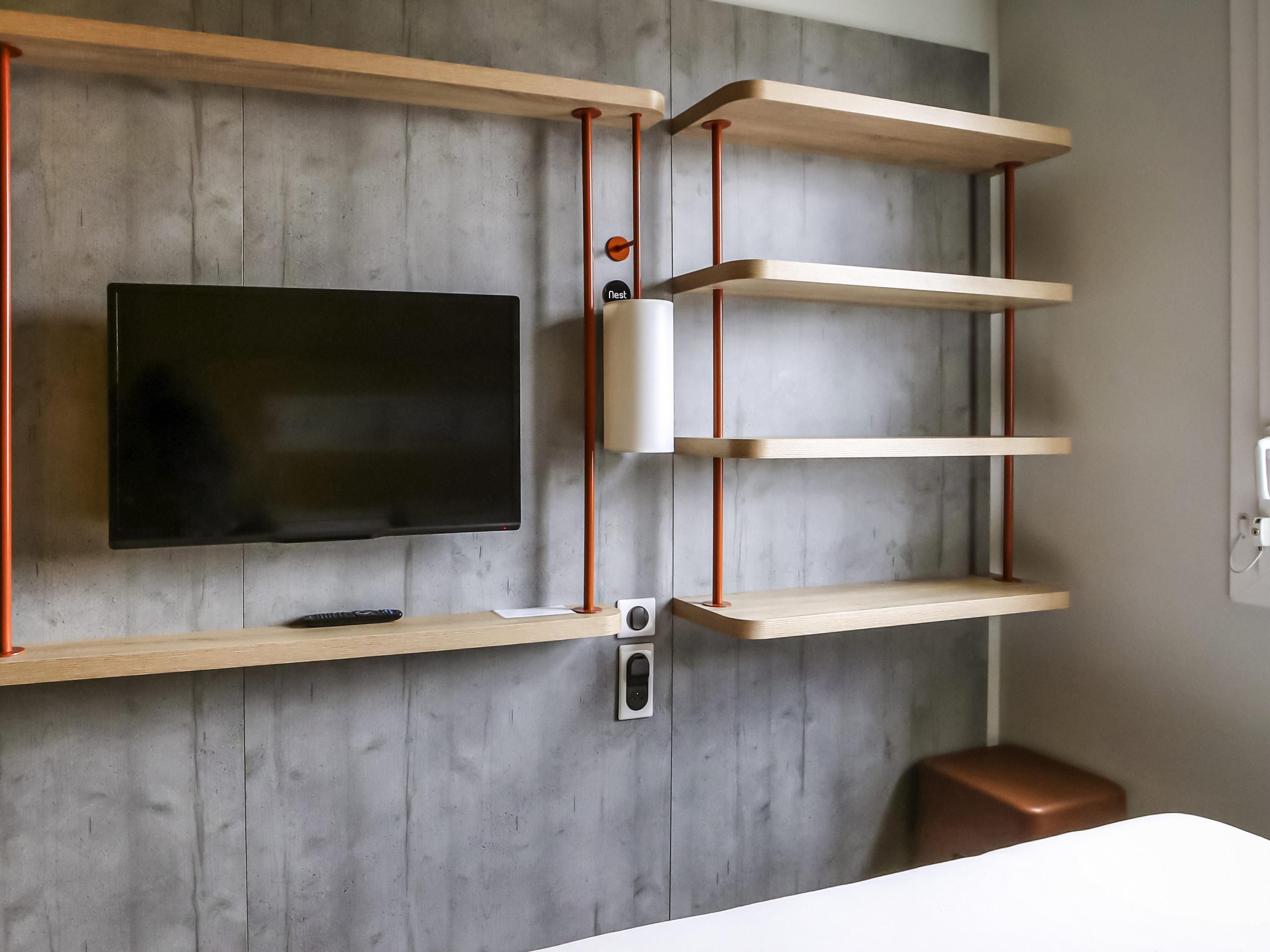 A modern room with a mounted TV, wooden shelves, and a brown leather ottoman.