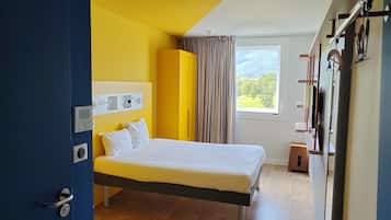 A modern hotel room with a bed, a window with a view, a wardrobe, and a door.