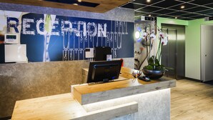 A reception desk with a computer, a plant, and a wall with the word "RECEPTION" in large letters. - Ibis Budget Saint Genis Pouilly Geneva (Saint-Genis-Pouilly)