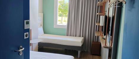 A room with a bed, a window with curtains, a bedside table, a wall-mounted TV, and a door with a handle.