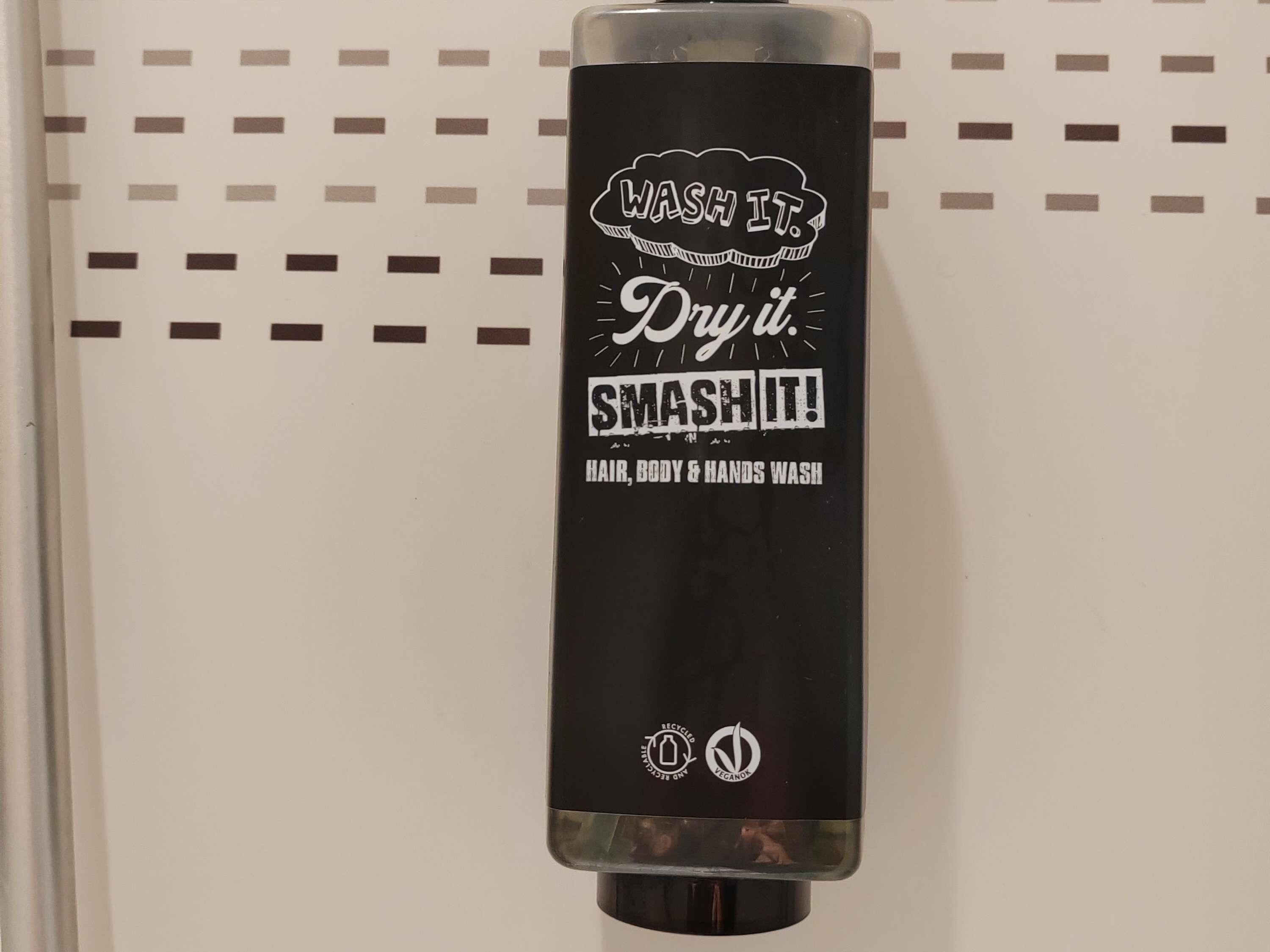 Een zwarte handdroger met witte tekst en logo's, bevestigd aan een muur met een paneelstructuur van gaatjes.
