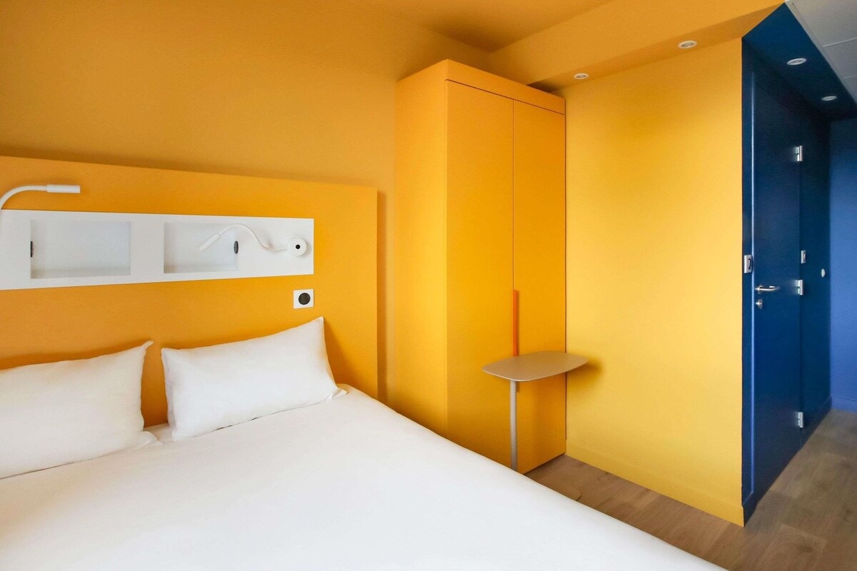 A hotel room with a bed, a bedside table, a wardrobe, and a door.