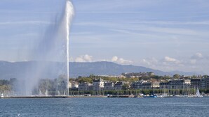 Une promenade au bord de l’eau avec une fontaine, des bateaux et des bâtiments en arrière-plan.