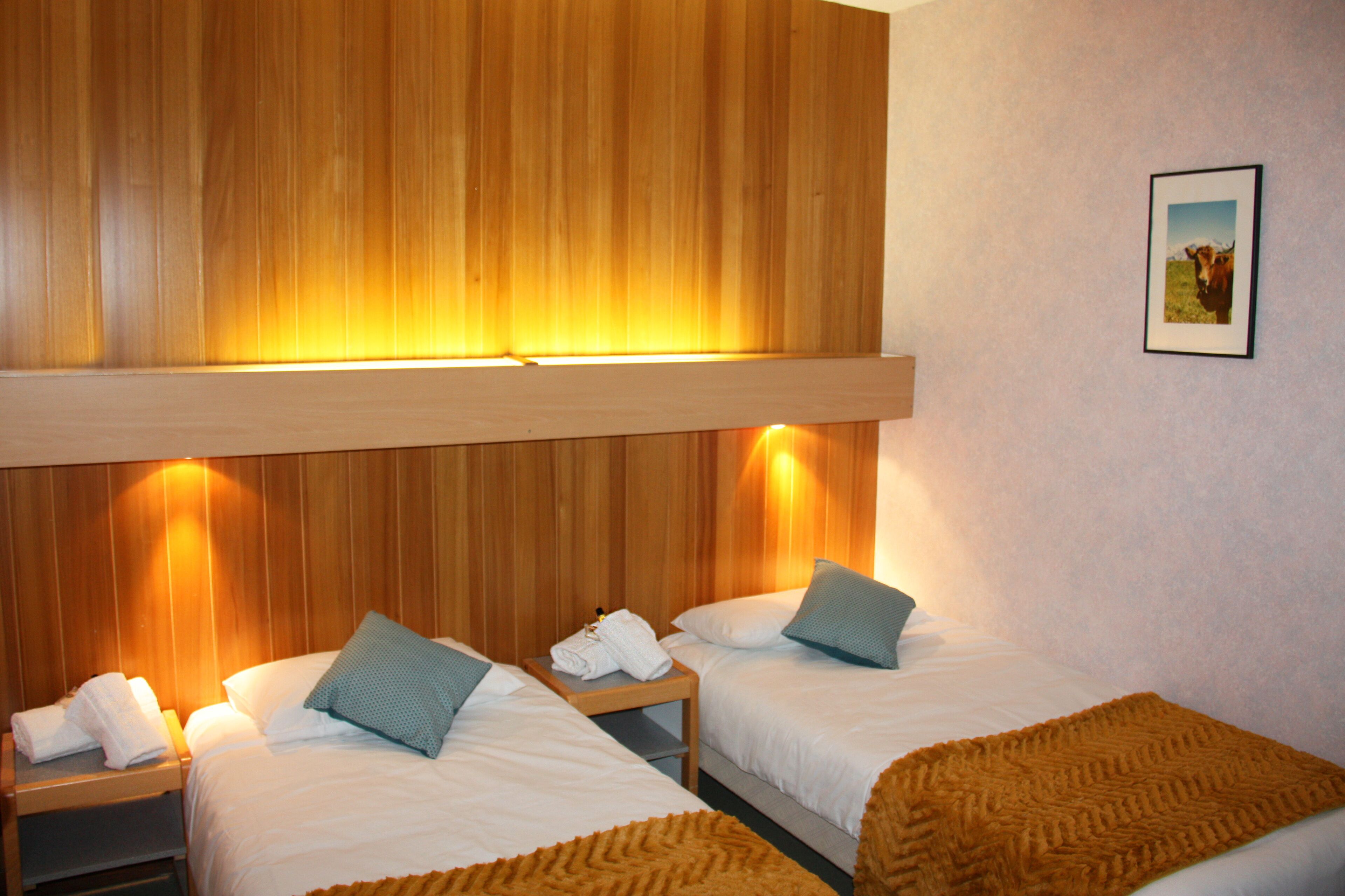 A hotel room with two beds, wooden headboard, and a framed picture on the wall.