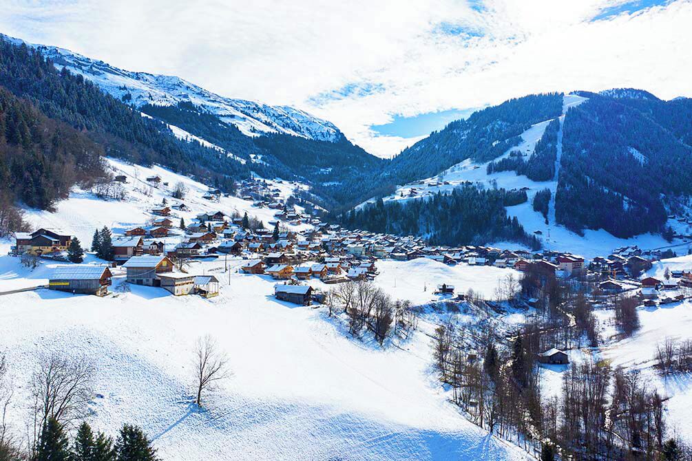 Un village enneigé, avec des maisons et des bâtiments dispersés dans une vallée.