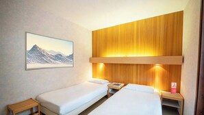 A hotel room with two single beds, a wooden headboard, a framed picture of a mountain, and a small table with a book. - Azureva Areches Beaufort (Beaufort)