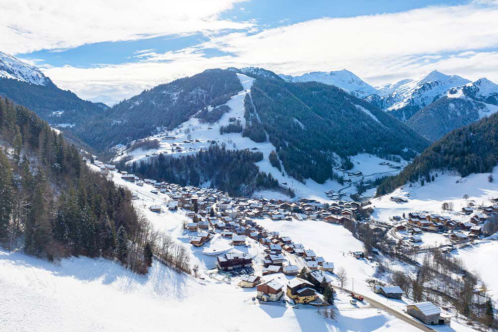 Un pueblo cubierto de nieve con casas y una pista de esquí en el valle.