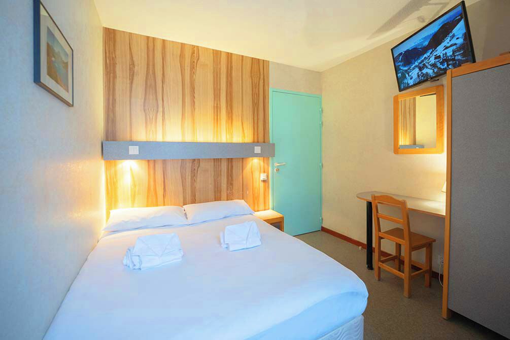 A hotel room with a bed, a desk, a chair, a television, and a door.