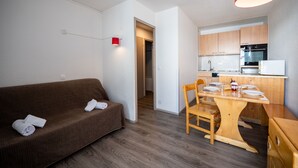 Un espacio habitable pequeño con un sofá marrón, una mesa de comedor de madera y una cocina con armarios y electrodomésticos de madera.