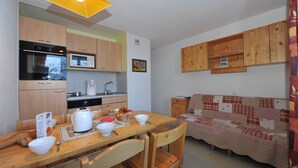Una cocina compacta con armarios de madera, microondas y cafetera. Hay una mesa de comedor con sillas y un sofá acolchado.