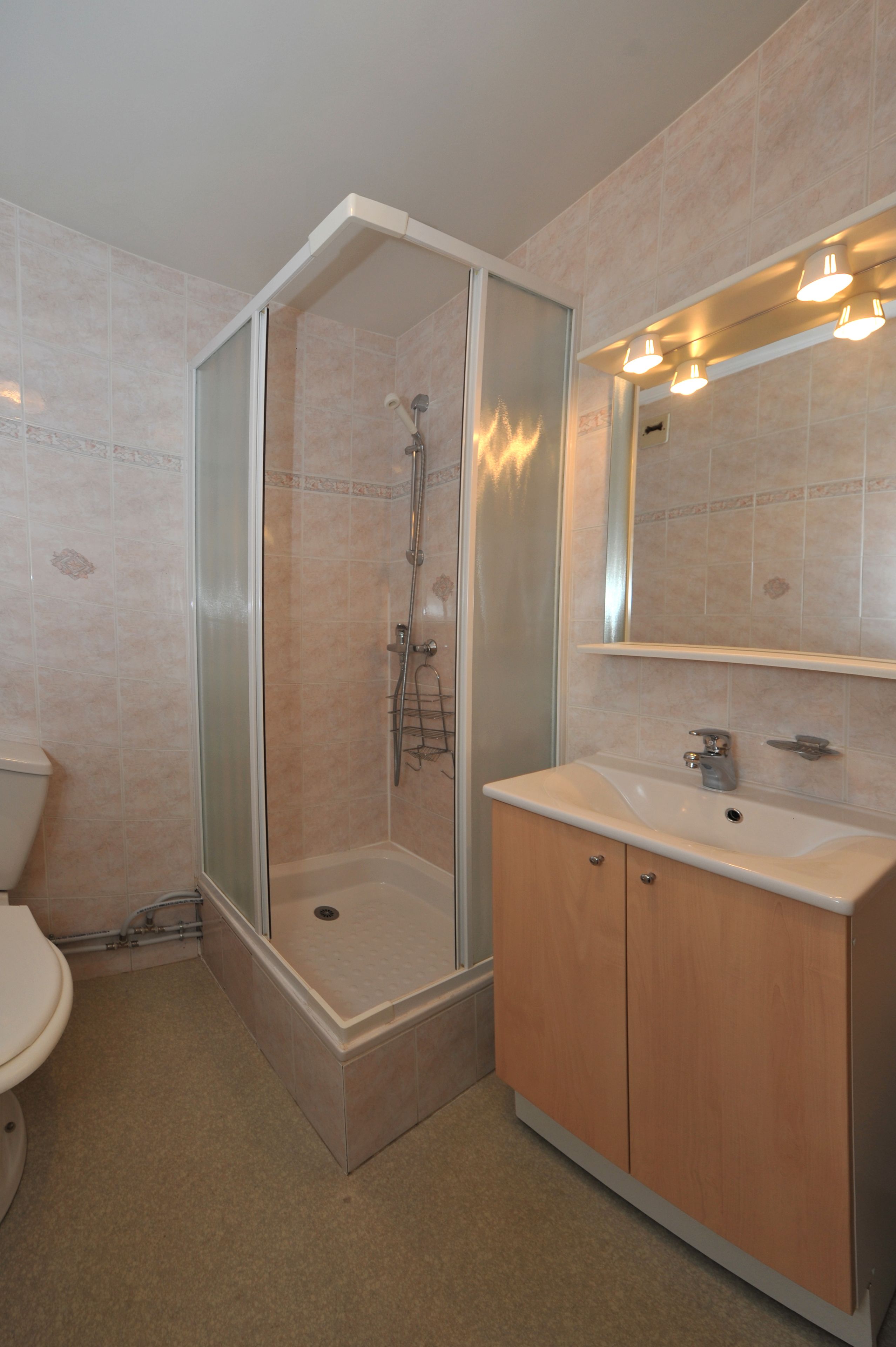A bathroom with a glass-enclosed shower, a sink with a mirror above, and wooden cabinets.