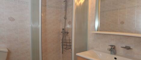 A bathroom with a glass-enclosed shower, a sink with a mirror above, and wooden cabinets.