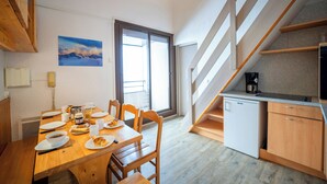Un comedor con mesa de madera, sillas y una disposición para el desayuno. Se observa una escalera con barandilla de madera que conduce a una zona de cocina.