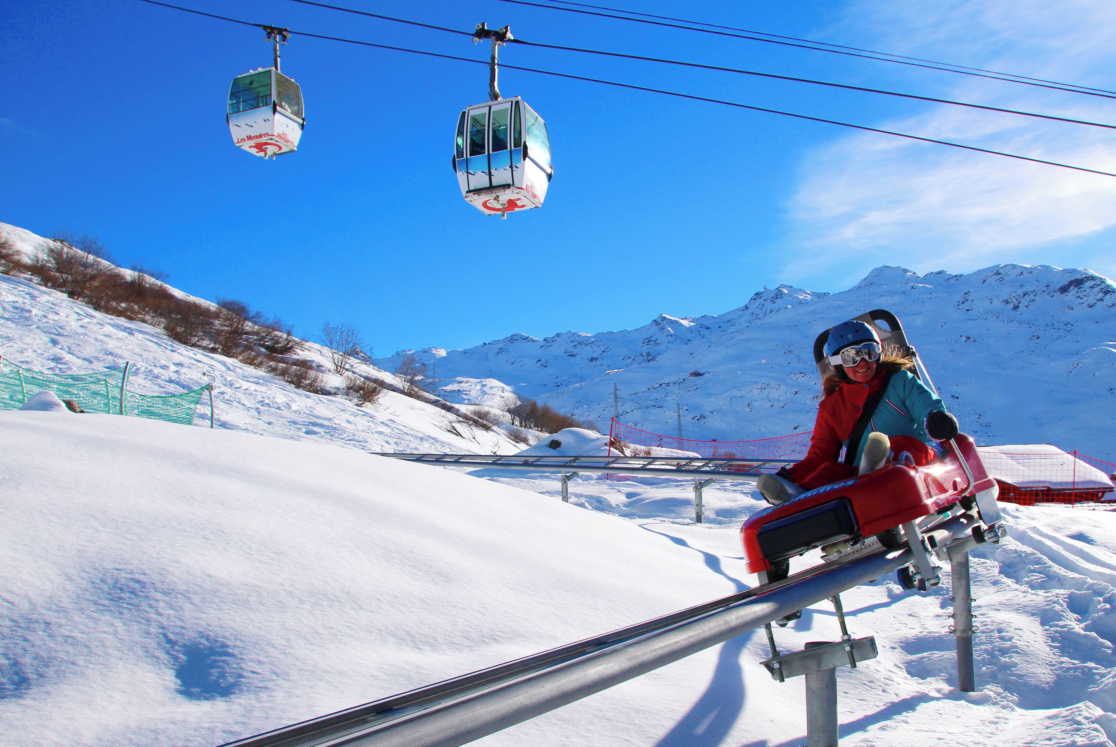 Un telesilla en una estación de esquí con laderas nevadas y montañas al fondo.