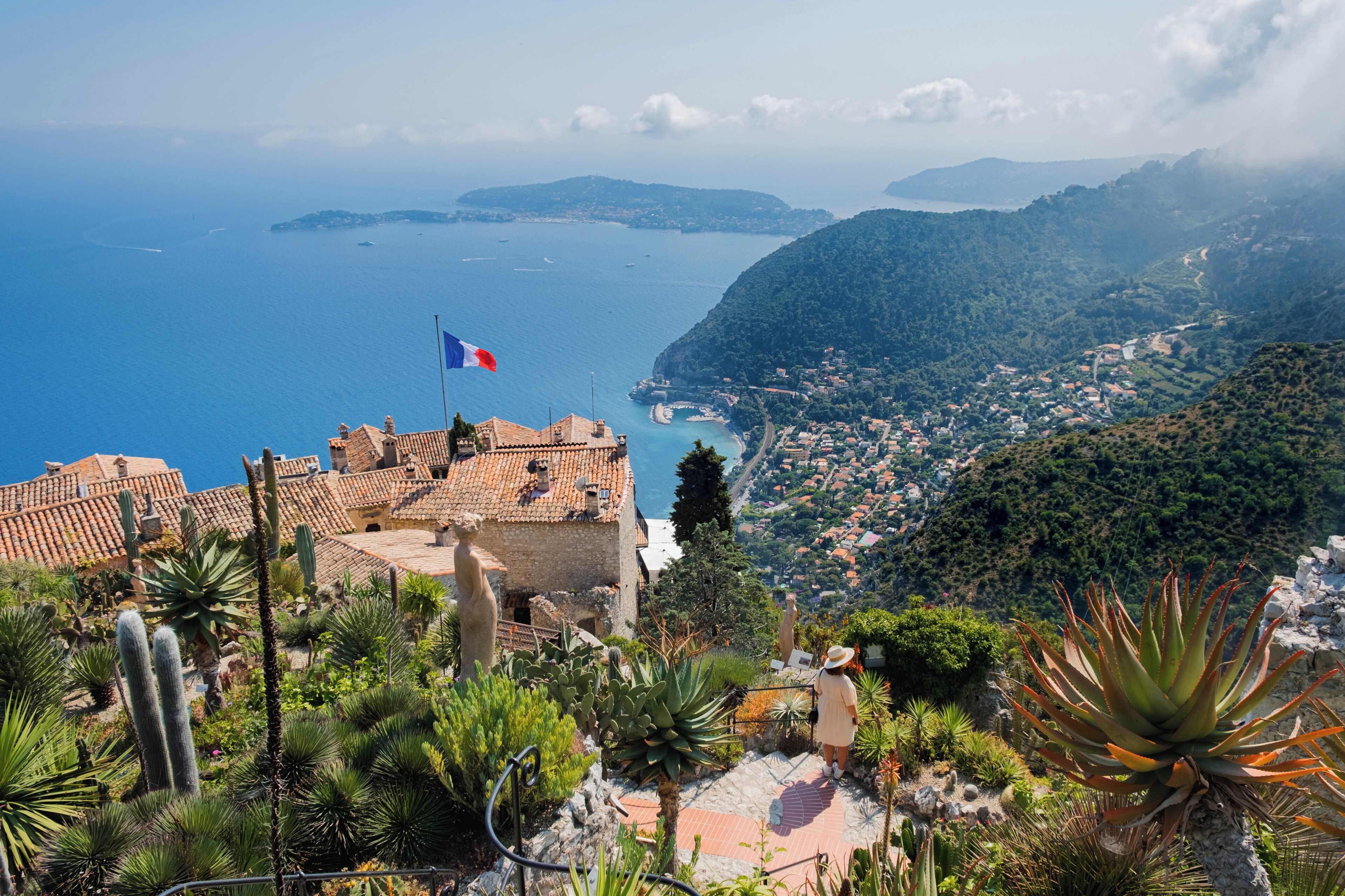 A coastal town with a view of the sea, a flag, and a building with a tiled roof.
