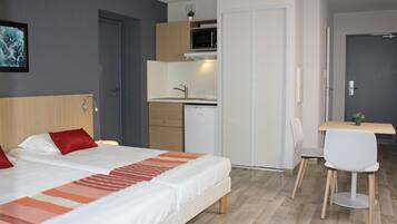 Une chambre d’hôtel équipée d’un lit, d’un bureau, d’une chaise, d’un four à micro-ondes et d’une petite kitchenette.