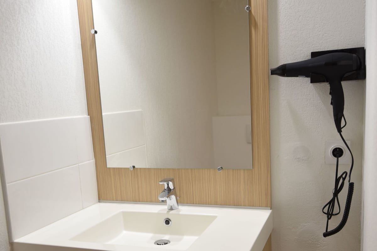 Une salle de bain avec un lavabo blanc, un meuble-lavabo en bois, un miroir et un sèche-cheveux fixé au mur.