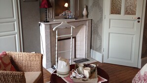 A cozy room with a wicker chair, a small table with a kettle and cups, a mirror, and a door with frosted glass panels. - Le Clos des Hautes Loges (Les Loges)