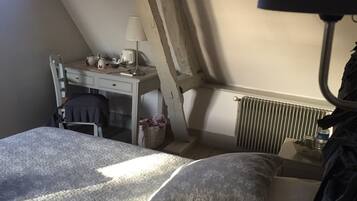 A bedroom with a sloped ceiling, a bed with patterned bedding, a desk with a lamp, and a radiator.