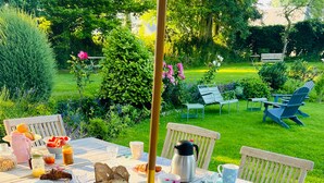 An outdoor dining area with a table set for breakfast, surrounded by chairs and a garden view. - Le Clos des Hautes Loges (Les Loges)