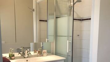 A bathroom with a white vanity, a large mirror, a glass shower enclosure, and a red bath mat.