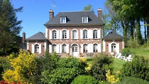 A large, two-story house with a symmetrical facade, multiple windows with shutters, and a well-maintained garden with various shrubs and flowers. - Le Clos des Hautes Loges (Les Loges)