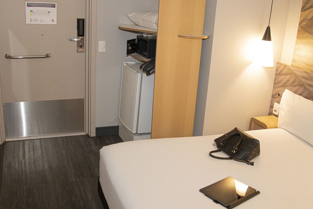 Une chambre d’hôtel équipée d’un lit, d’une table de chevet, d’une lampe et d’un petit réfrigérateur.