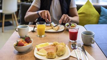 Een ontbijttafel met eten op een bord, een fruitschaal, een glas sinaasappelsap en een kop koffie.