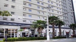 Un hotel de varios pisos con una fachada moderna, una entrada cubierta y palmeras en primer plano.