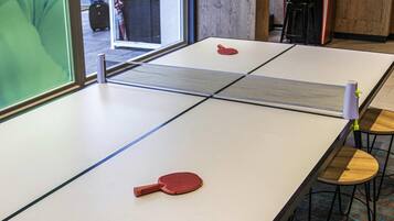 Une table de ping-pong avec deux raquettes et un filet au milieu. Il y a deux tabourets en bois avec des pieds en métal.