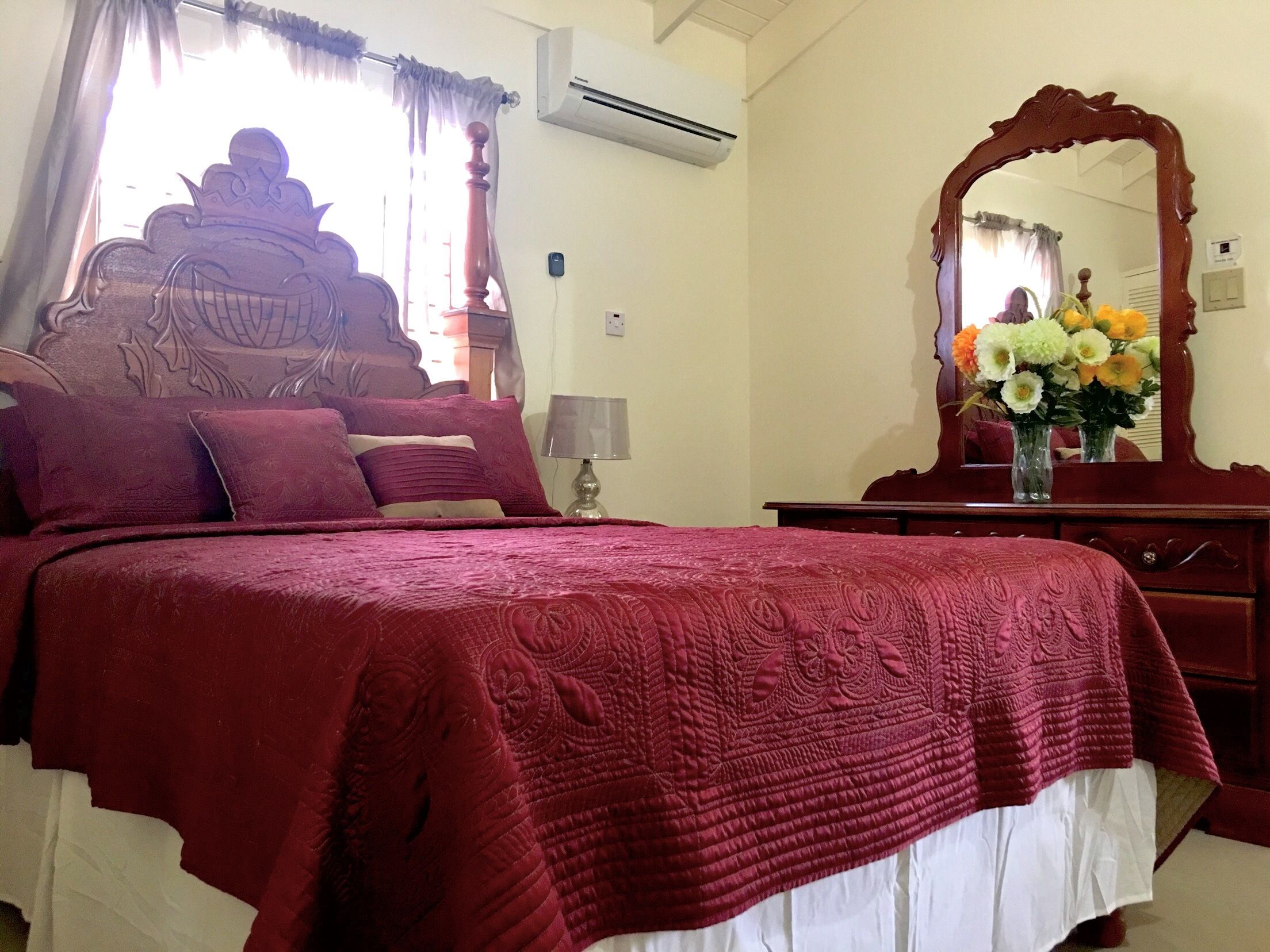 A bedroom with a large bed, a wooden headboard, a mirror, a dresser, and a vase with flowers.